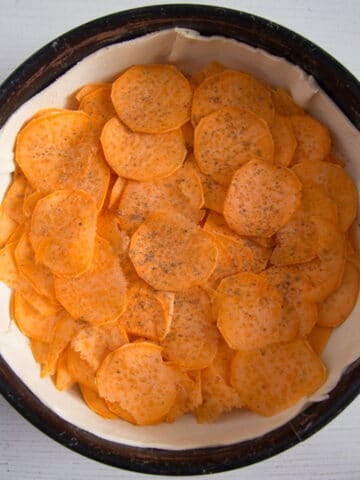 thin slices of sweet potatoes in a baking dish preparing for making a pie.