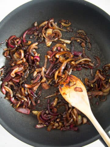 caramelizing red onions in a pan and stirring them with a wooden spoon.