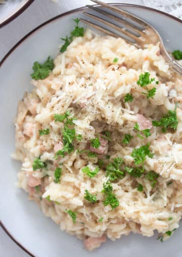 creamy risotto with turkey leftovers, bacon, parmesan and parsley on a small white plate.