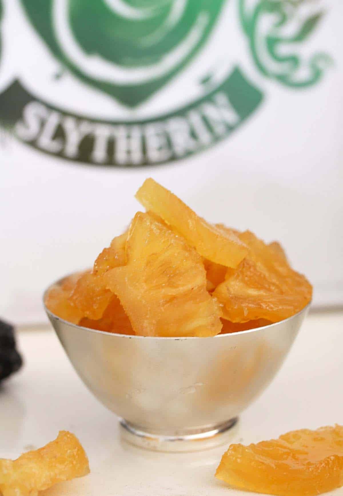 slughorn's crystallized pineapple pieces in a small bowl with slytherin logo behind.