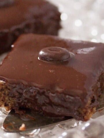 close up of a slice of chocolate traybake with shiny glaze on a cake lifter.
