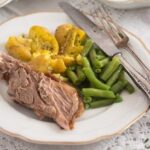 sliced meat on a plate with potatoes and green beans