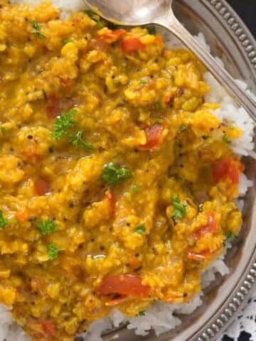 yellow moong dal served on rice on a silver plate.