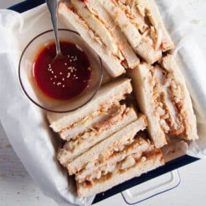 many half tonkatsu sandwiches in a baking dish with a bowl of sauce.