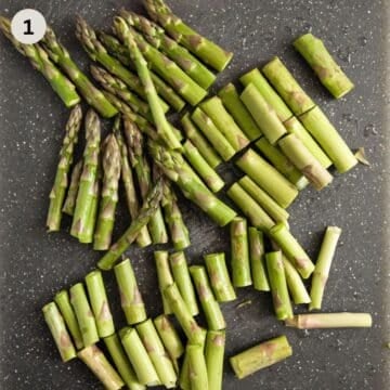 asparagus spears cut into smaller pieces on a dark cutting board.
