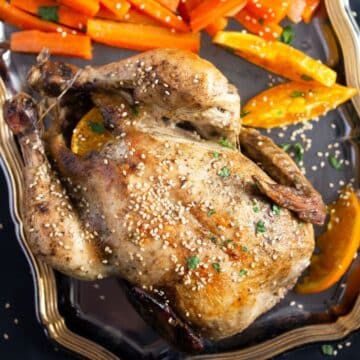 orange roast chicken sprinkled with sesame seeds on a platter.