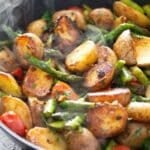 stirring pan-fried asparagus and potatoes in the skillet with a wooden spoon.