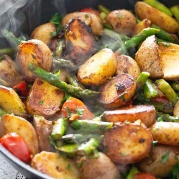 stirring pan-fried asparagus and potatoes in the skillet with a wooden spoon.