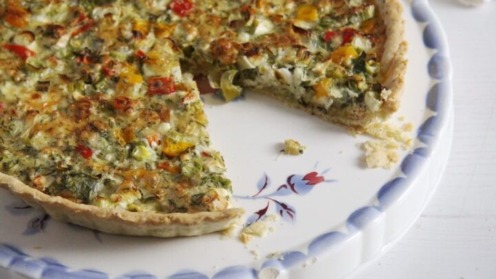 quiche with a slice missing on a vintage platter with blue flowers.