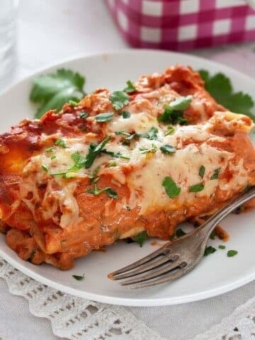 two red sauce chicken enchiladas on a small plate with a fork.