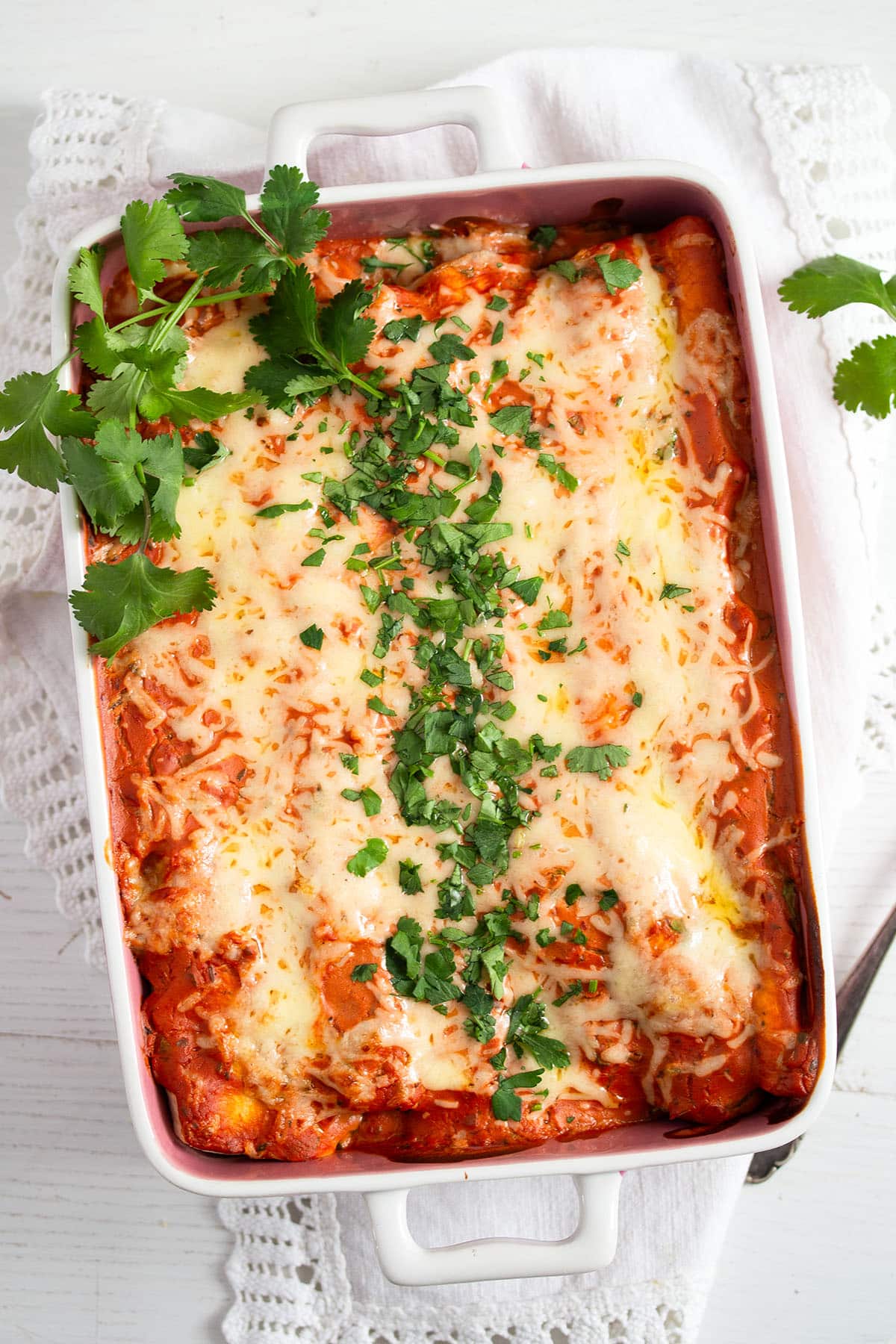 red sauce and sour cream enchiladas sprinkled with cilantro in a baking dish.