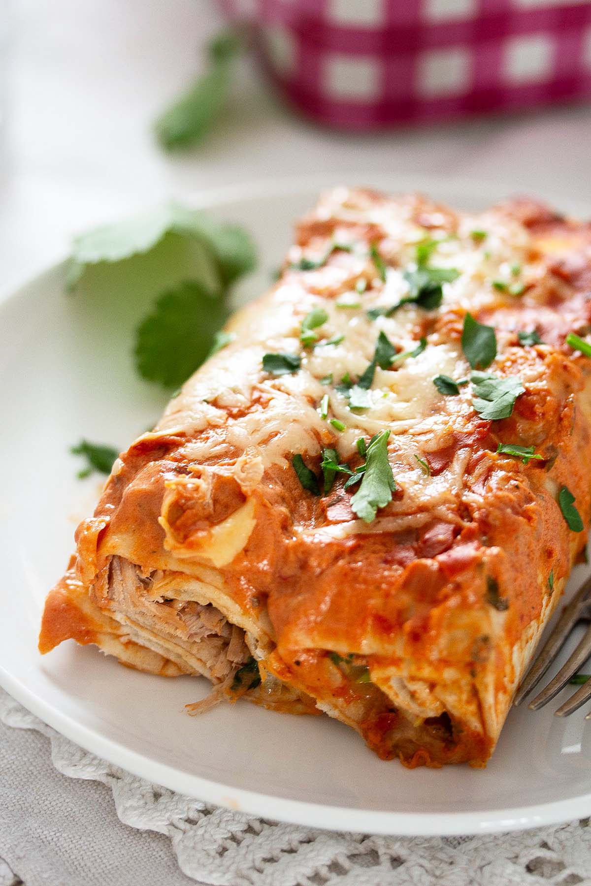 two large chicken enchiladas cooked in sour cream red sauce and sprinkled with cheese and cilantro.