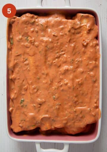 covering chicken enchiladas with tomato red sauce before baking.