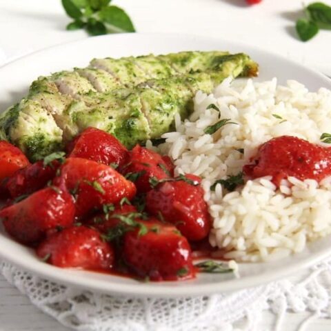 chicken with strawberries and rice being served on a white plate