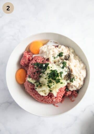 unmixed mealoaf mixture with beef, eggs, soaked bread and seasoning in a bowl.