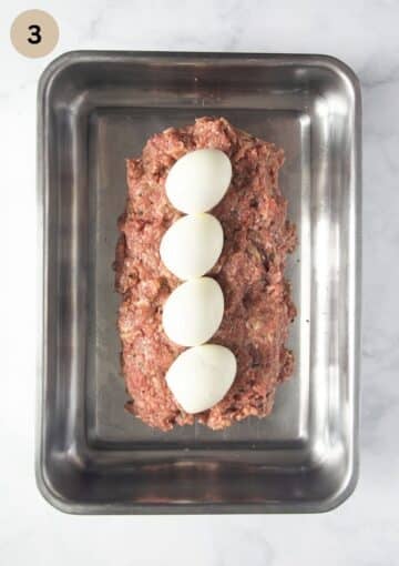 adding four hard-boiled eggs to a loaf of ground beef to make meatloaf with eggs inside.