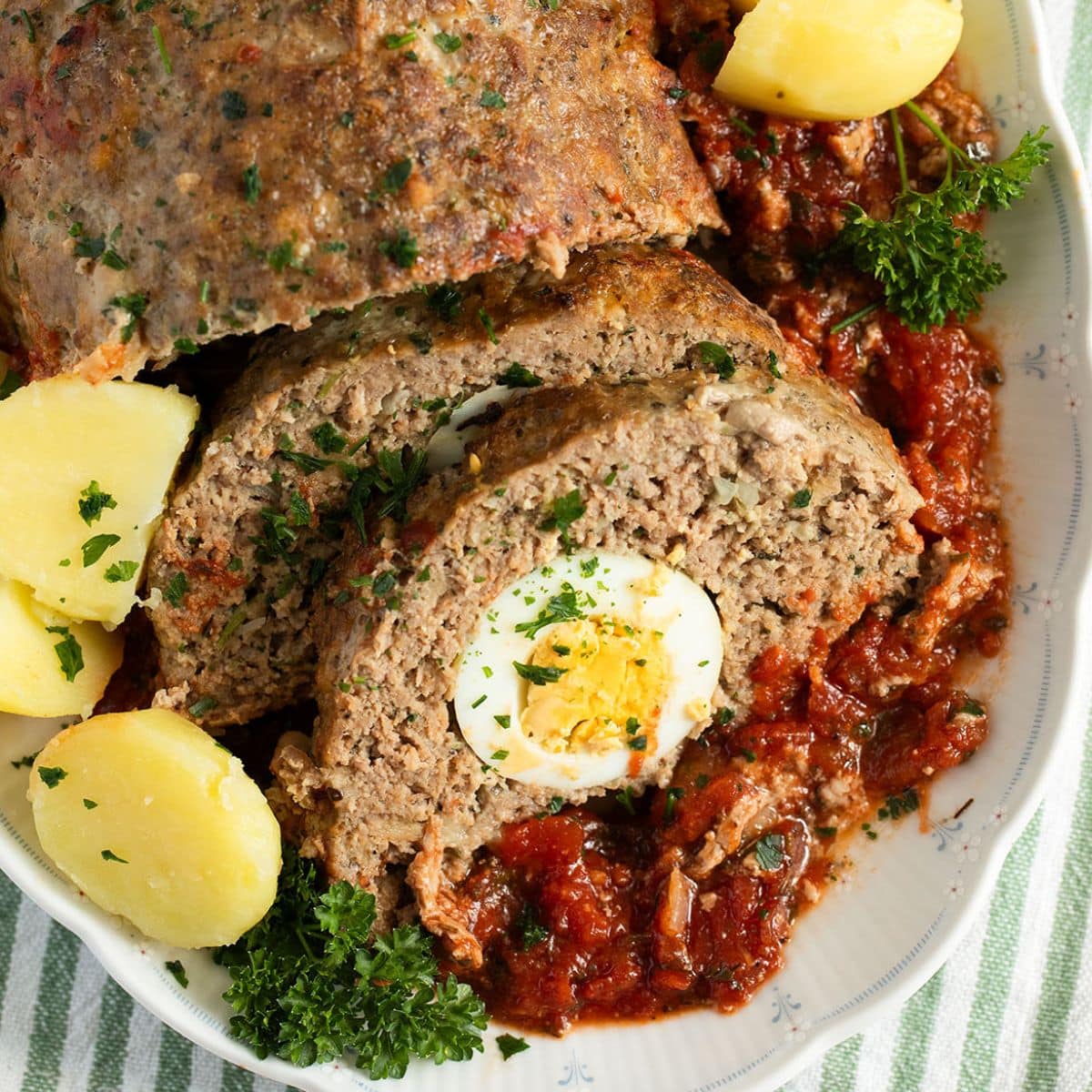 meatloaf with egg inside cut into slices and served with potatoes and tomato sauce.