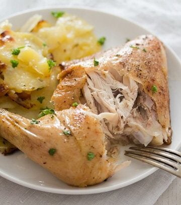 a chicken quarter with fall-off the bone meat and potatoes on a plate