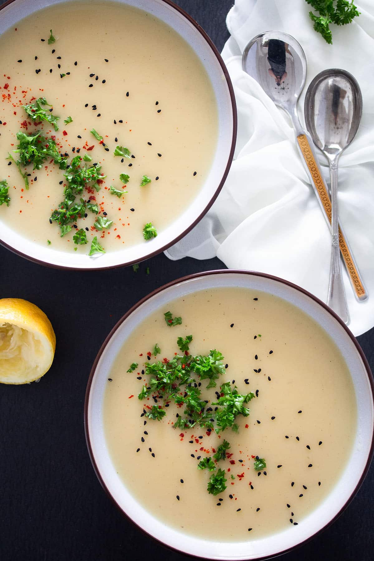 two bowls of creamy kohlrabi soup sprinkled with parsley, nigella seeds and chili flakes.