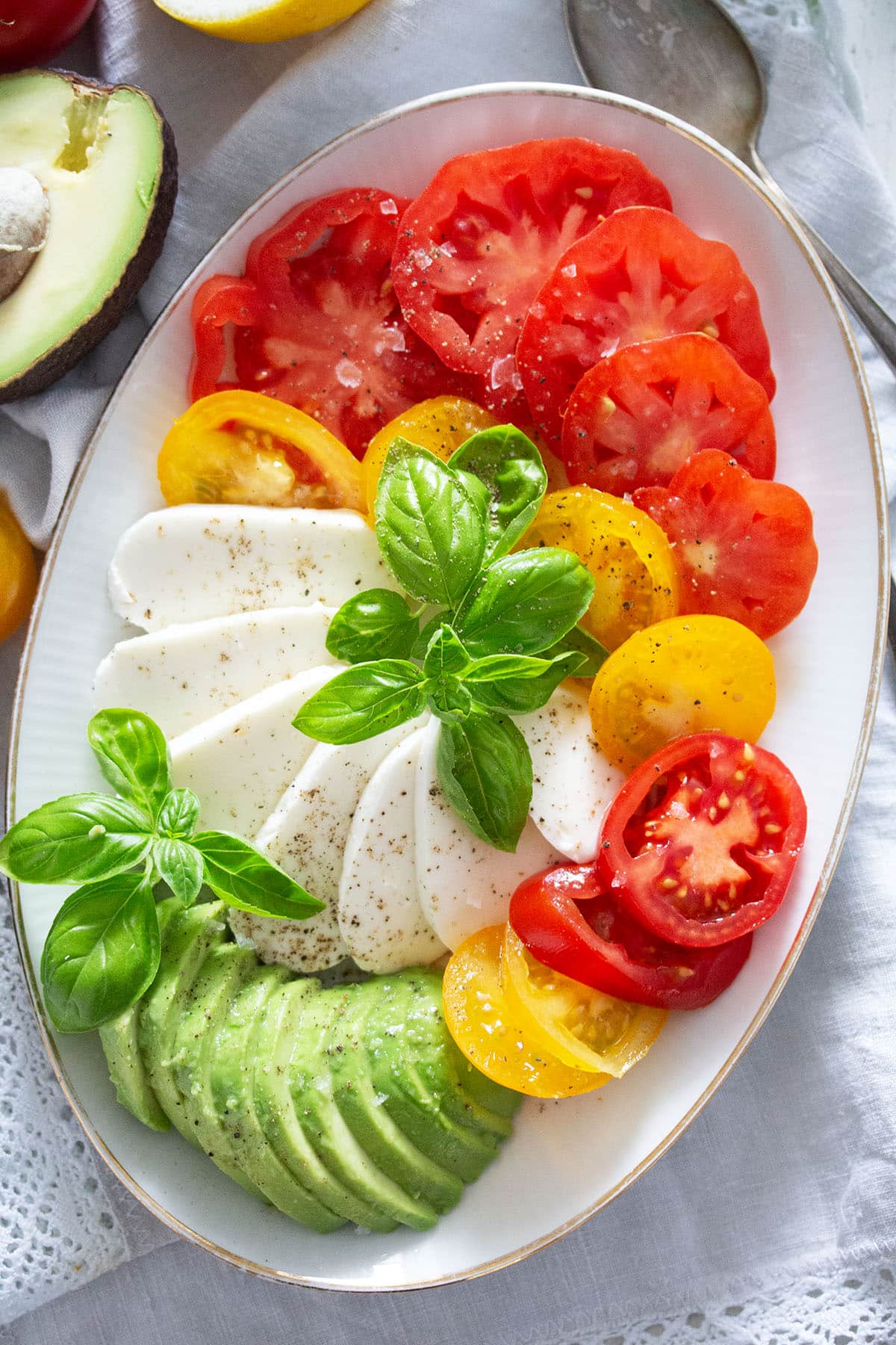 salad tricolore with mozzarella, avocado, tomatoes, and basil on an oval platter.