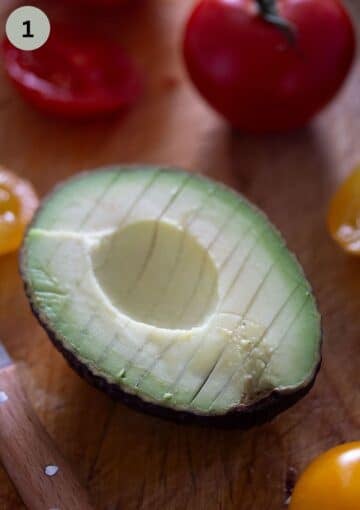 one avocado half sliced in the shell on a wooden board.