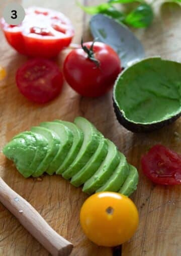 sliced avocado, an empty avocado shell and a few tomatoes on a board.