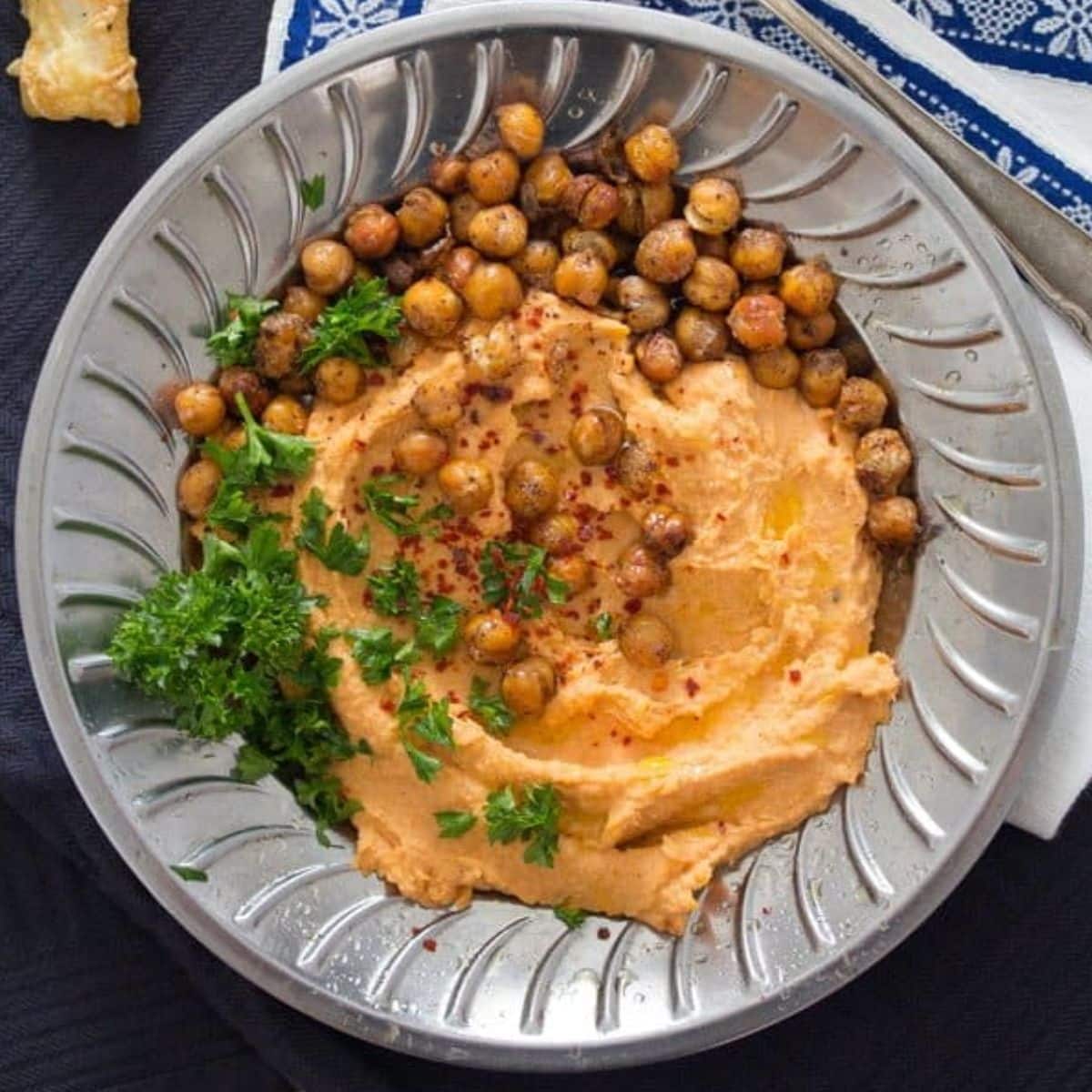 roasted red pepper white bean dip topped with roasted chickpeas and parsley on a silver plate.