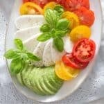 mozzarella tricolore salad with slices of tomato, avocado, and mozzarella on a platter.