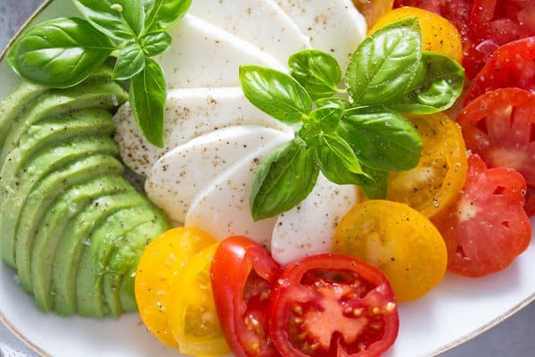 tomato avocado mozzarella salad sprinkled with pepper and topped with basil leaves