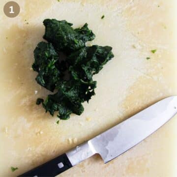 wilted chopped spinach and a large knife on a cutting board.