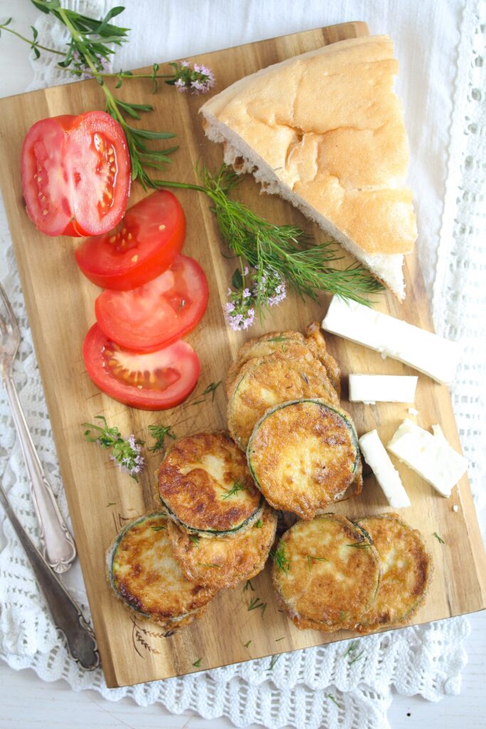 wooden board with fried zucchini, tomatoes, bread and feta