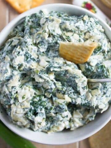 no-bake spinach artichoke dip in a bowl with a cracker and a spoon in it.