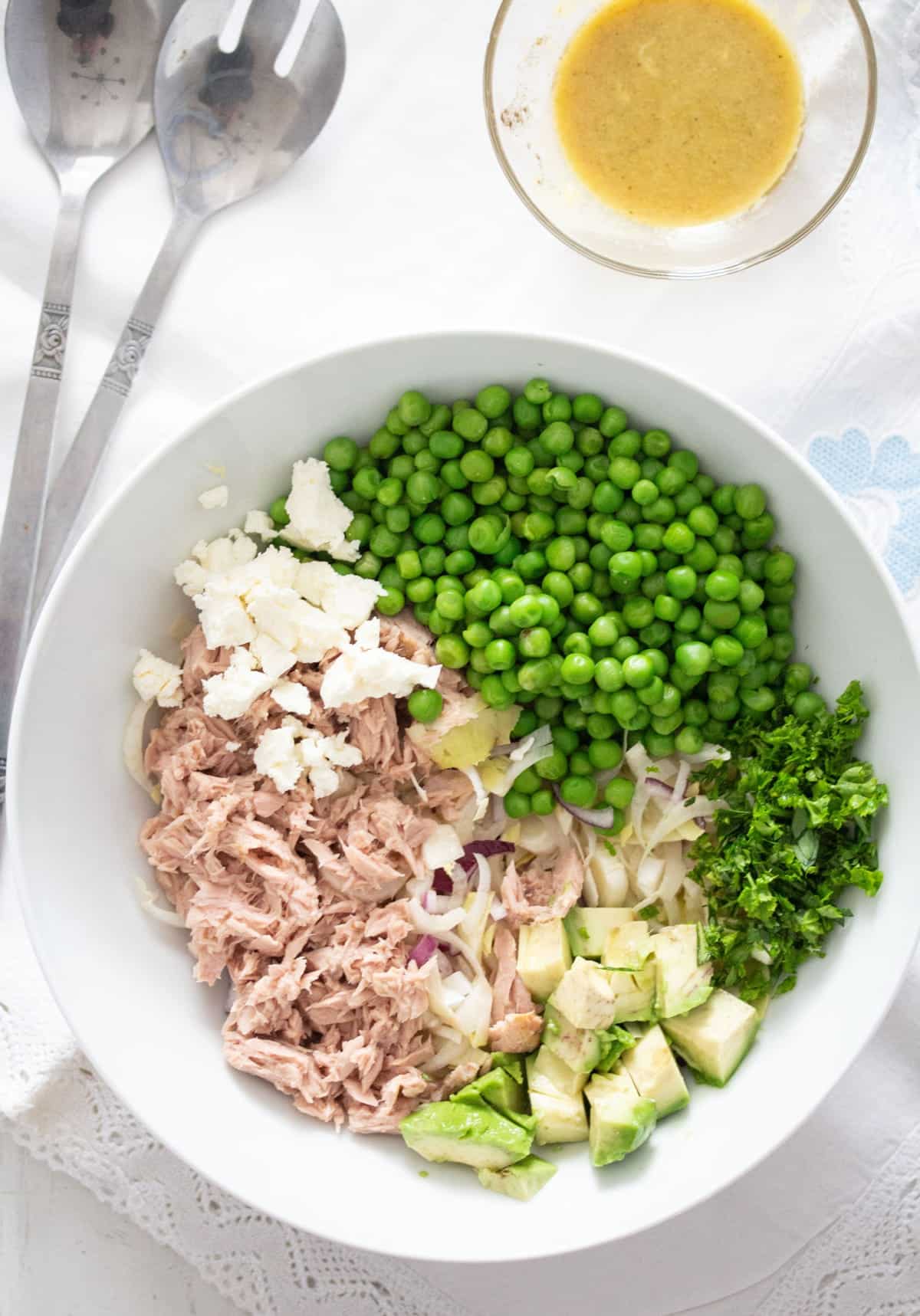 unmixed ingredients for salad: tuna, feta, peas, avocado in a bowl.