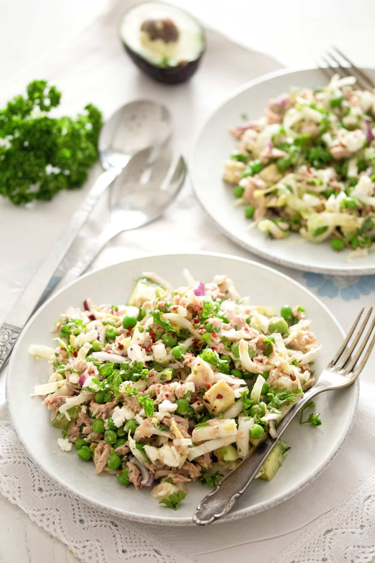 two plates with salad with feta, tuna, chicory and a cut avocado behind.