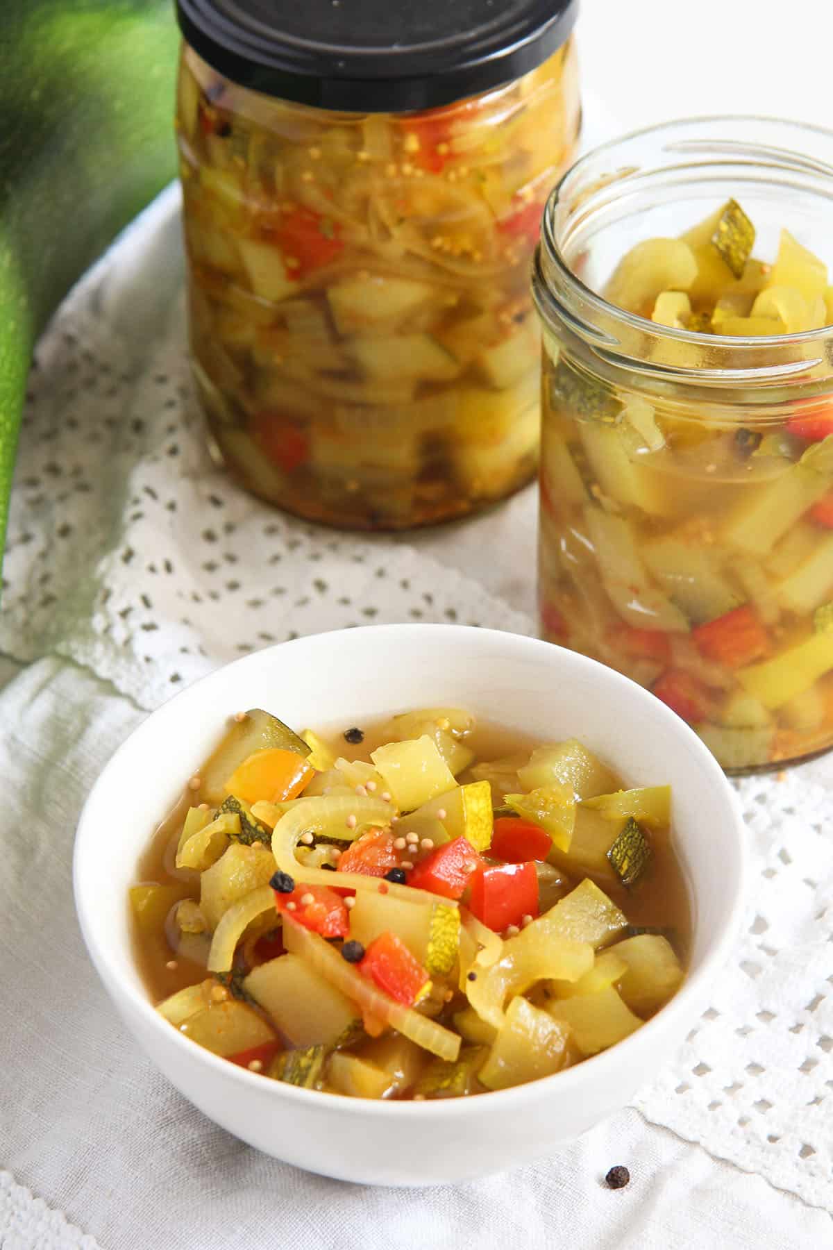 a bowl and two jars full of sweet and sour zucchini pickles.