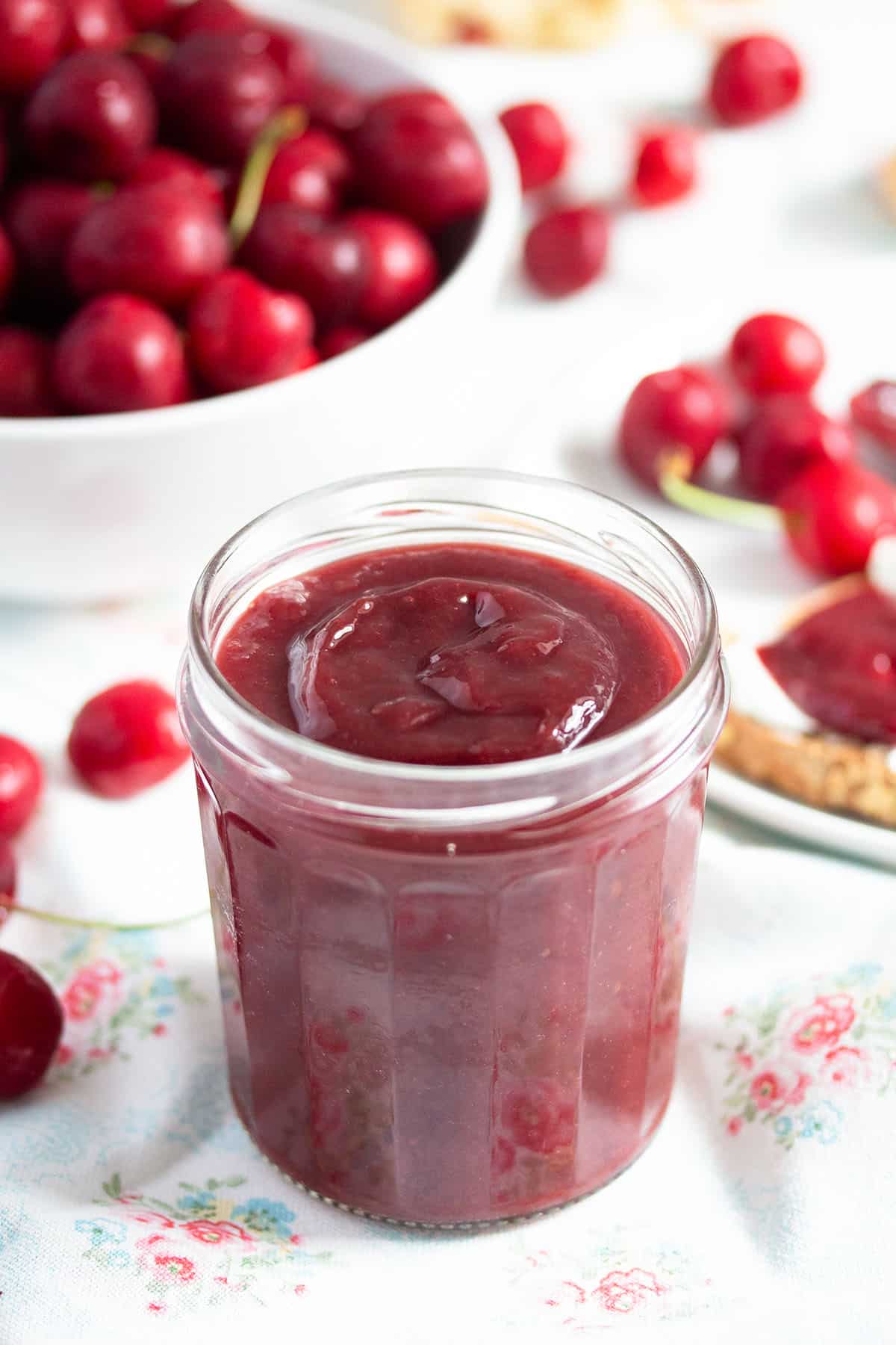 smooth cherry butter in a jar and many fresh cherries behind it.
