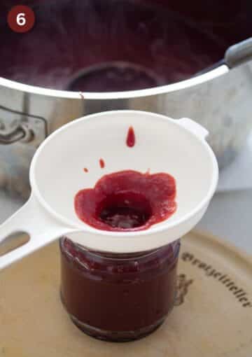filling cherry butter in a jar using a jam funnel.