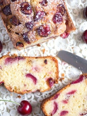 cherry loaf cake sliced on a vintage cloth with a knife and fresh fruit around it.