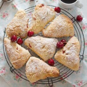 seven cherry scones sprinkled with powdered sugar on a wire rack.