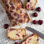 cherry loaf cake sliced with cherries and a knife beside it.