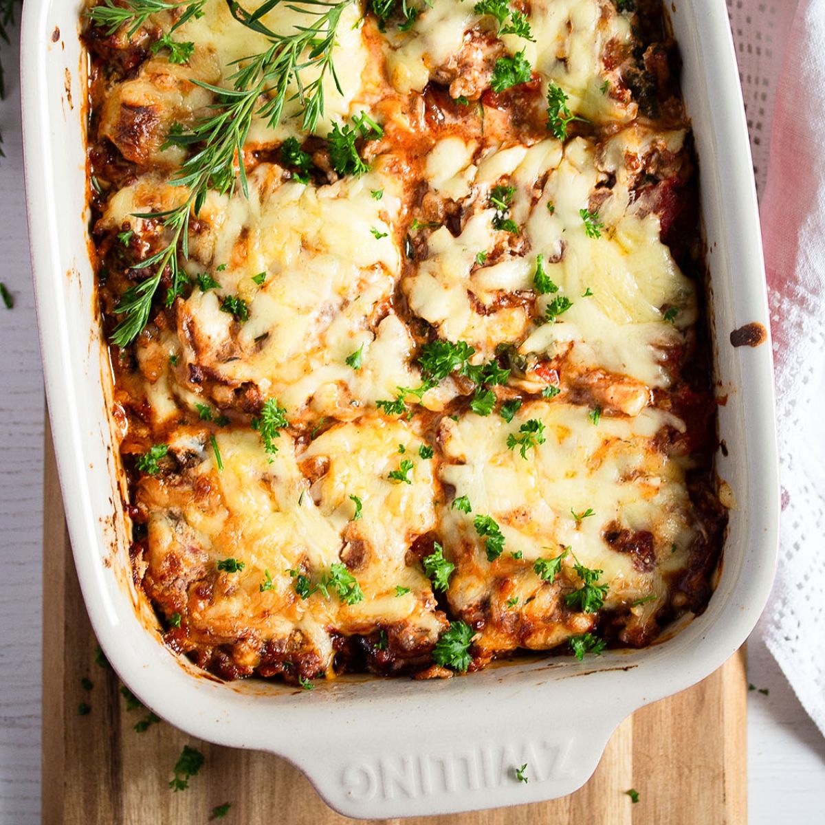 ground beef and zucchini casserole in a baking dish garnished with fresh herbs.