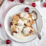 kirschmichel served with vanilla sauce on a small vintage plate with a spoon and cherries around it.