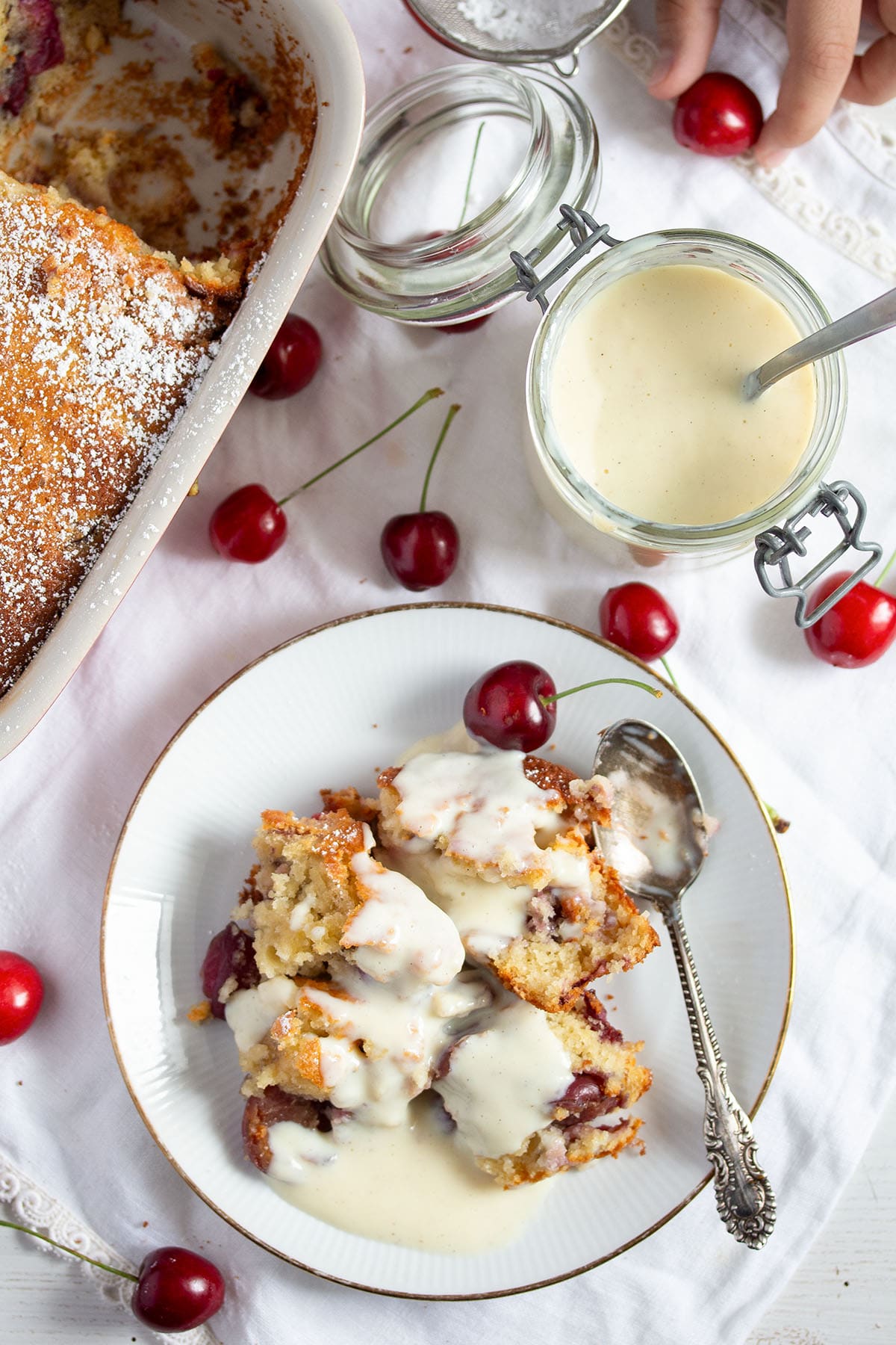 kirschmichel covered with vanilla sauce on a plate, more sauce in a jar, cherries and a child's hand around it.