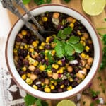 mexican bean salad with corn in a bowl with serving spoons in it.