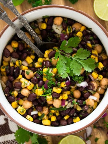 mexican bean salad with corn in a bowl with serving spoons in it.