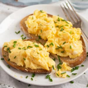 two sourdough toast slices piled with fluffy scrambled eggs.