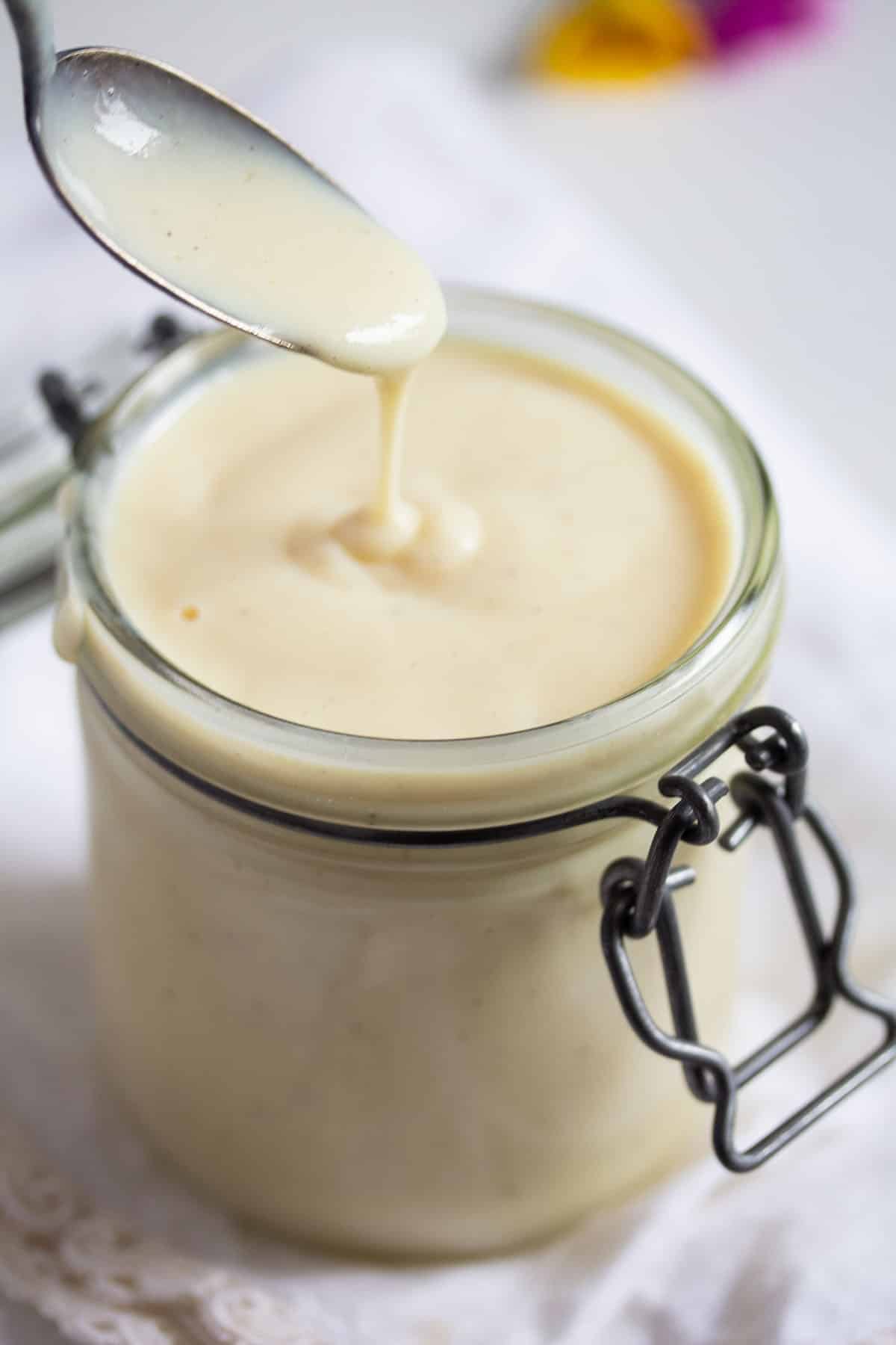 dripping vanilla sauce from a spoon back into a jar.