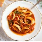 calamari stew in a white deep plate with golden edge with a spoon in it.