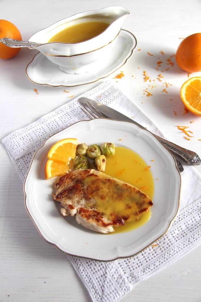 a plate with chicken breast with orange sauce and the sauce container behind it.