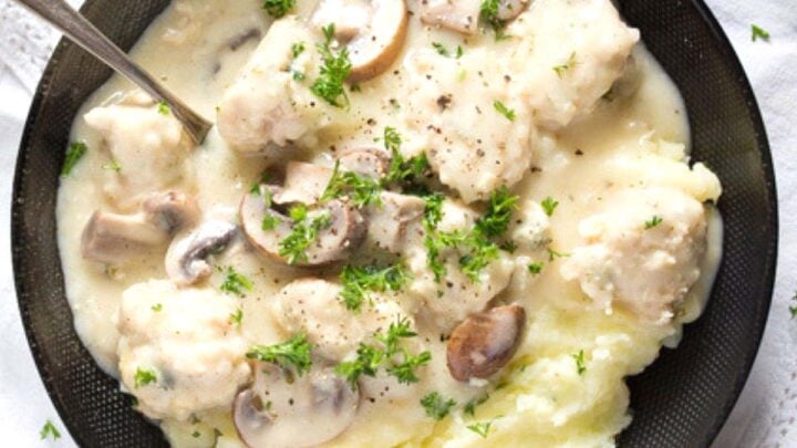 chicken meatballs in creamy sauce served with mashed potatoes in a black bowl.